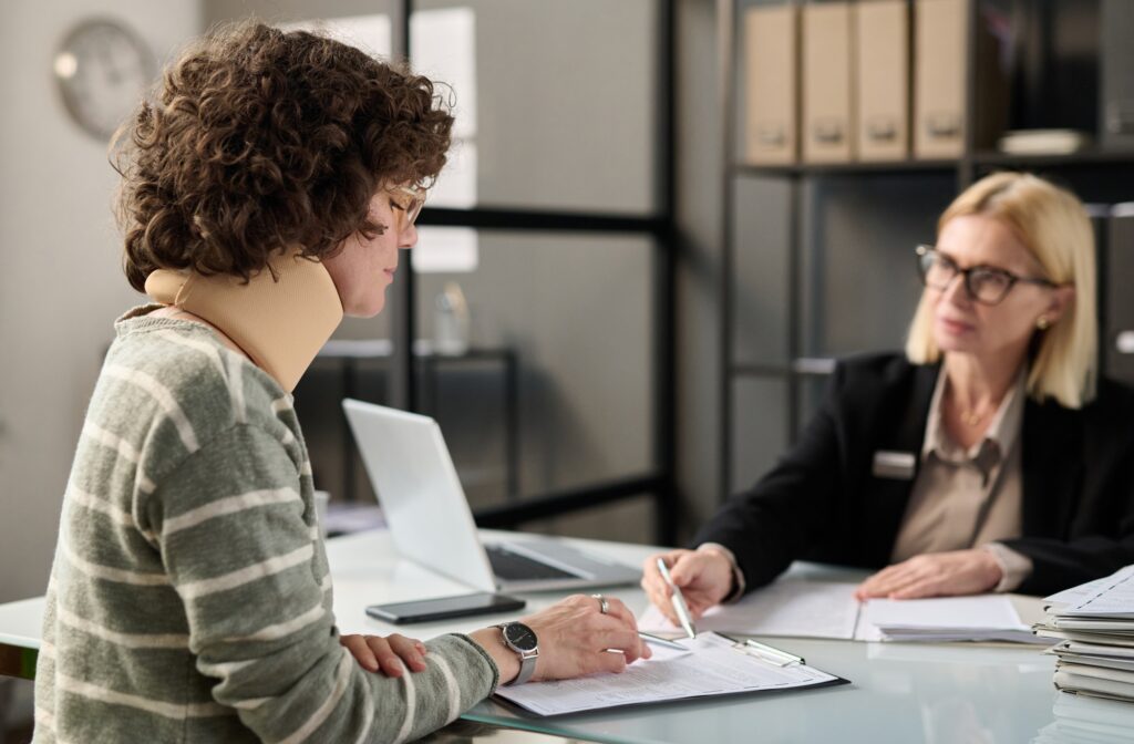 a woman sitting at a desk with a woman in a neck brace