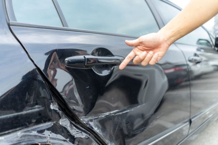 person pointing to damage on a car’s bumper