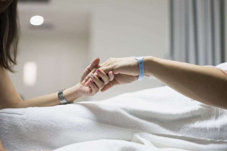 person holding patient’s hand in hospital bed