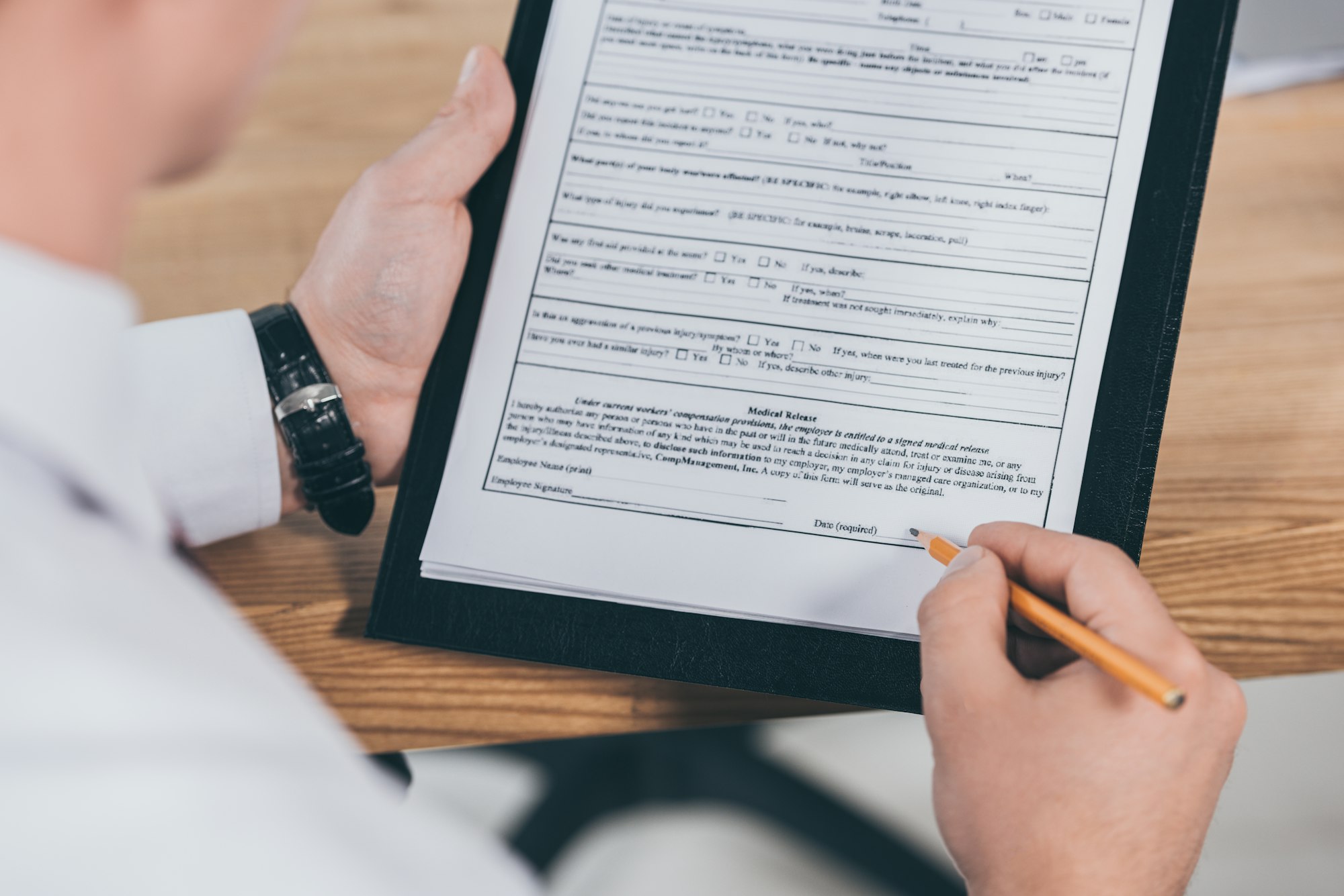 cropped view of businessman putting signature on compensation claim form at workspace