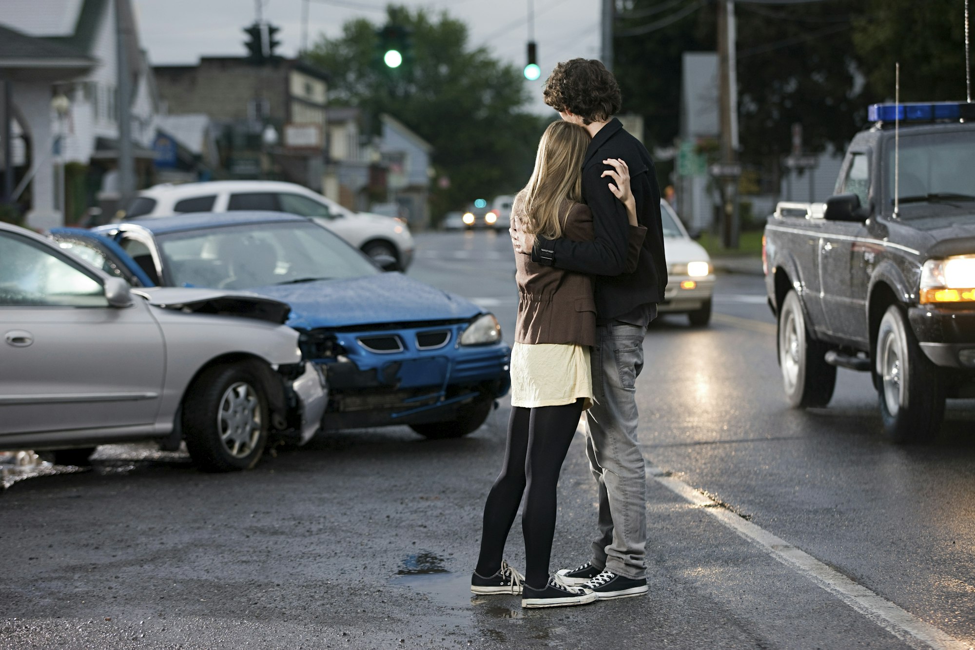 Embrace amidst chaos Two people sharing a moment on a street with a car accident in the background