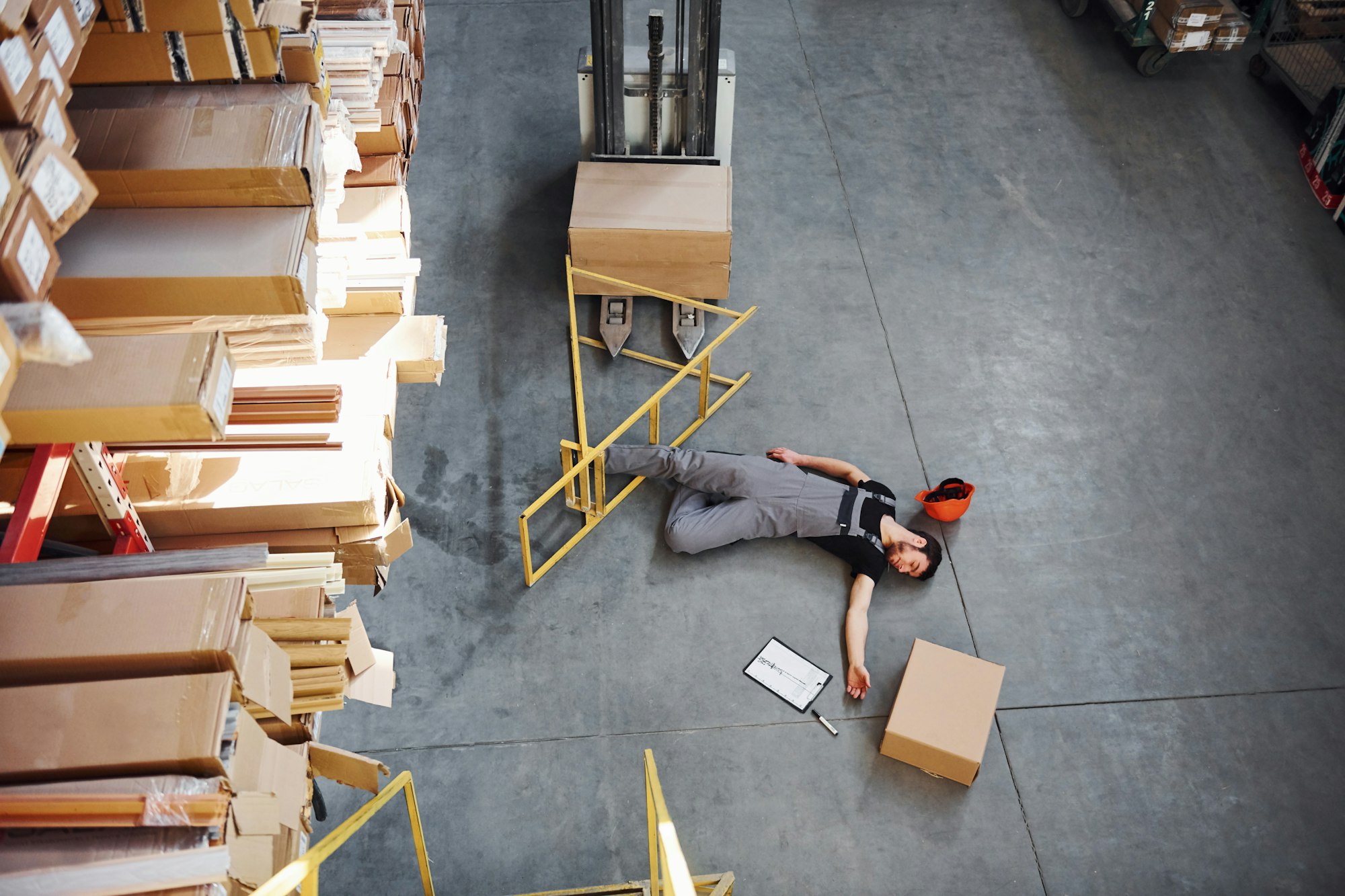 Warehouse worker after an accident in the storage. Man in uniform lying down on the ground