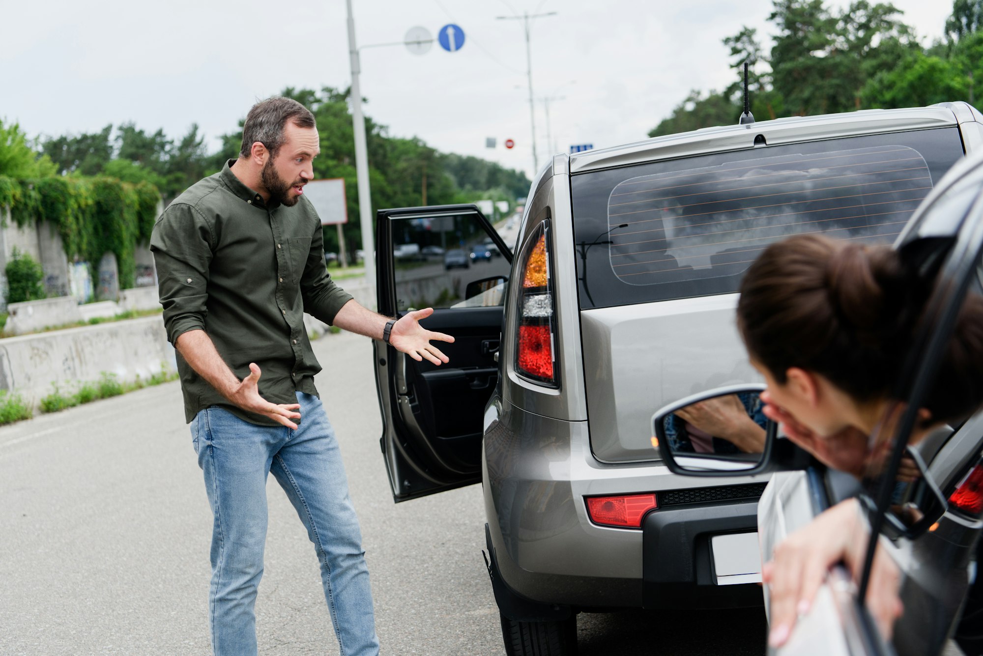 male and female drivers gesturing after car accident on road