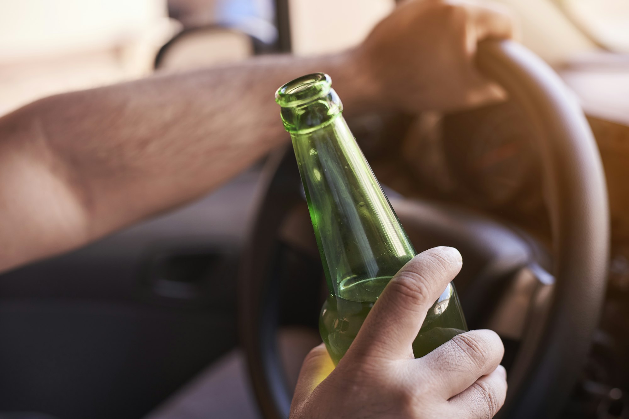 Man driving a car while holding a bottle of beer. Drunk diving, unsafe driving concept