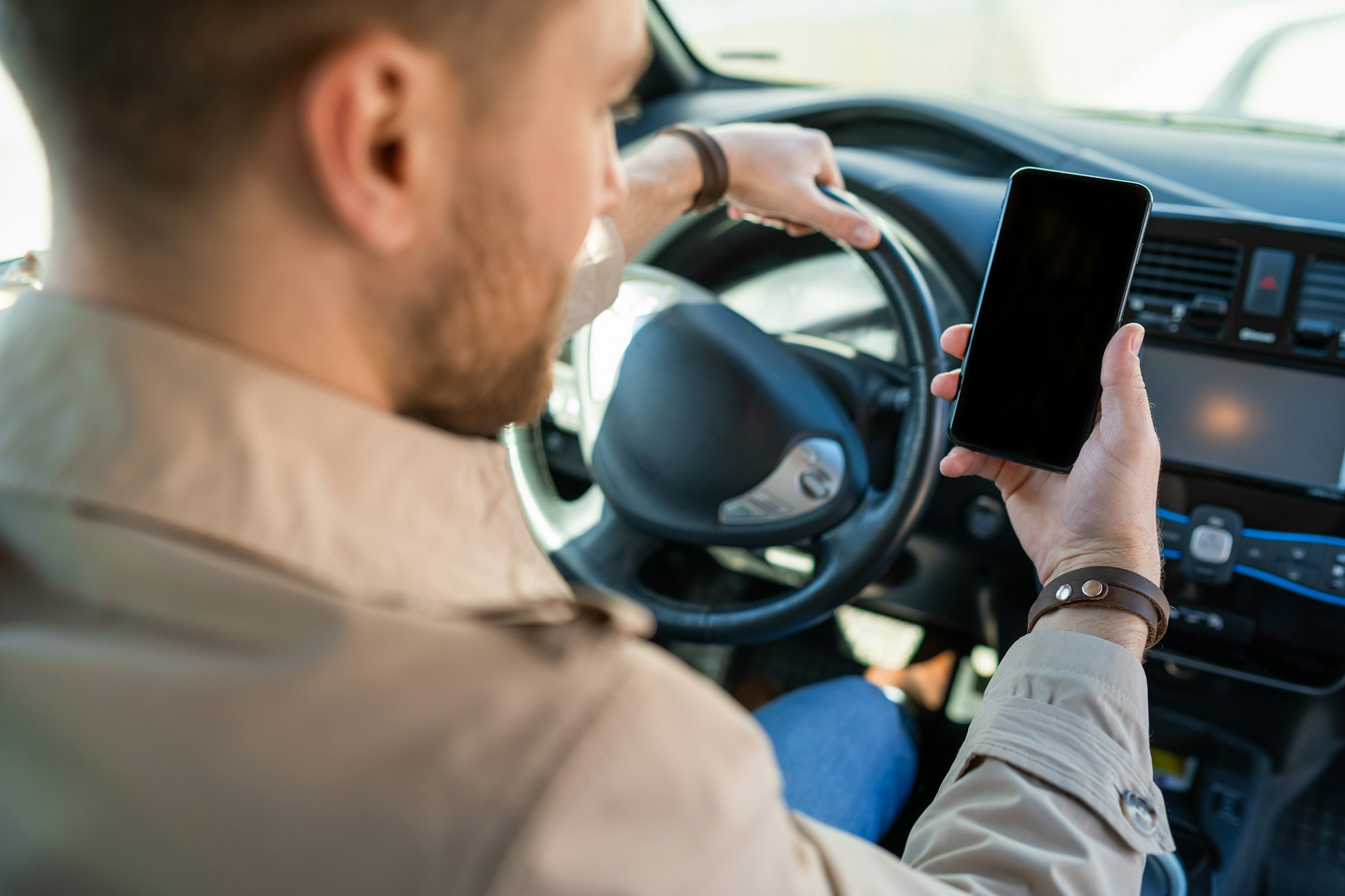 Man driving car with a smartphone in hand. Male looking at the phone screen while driving