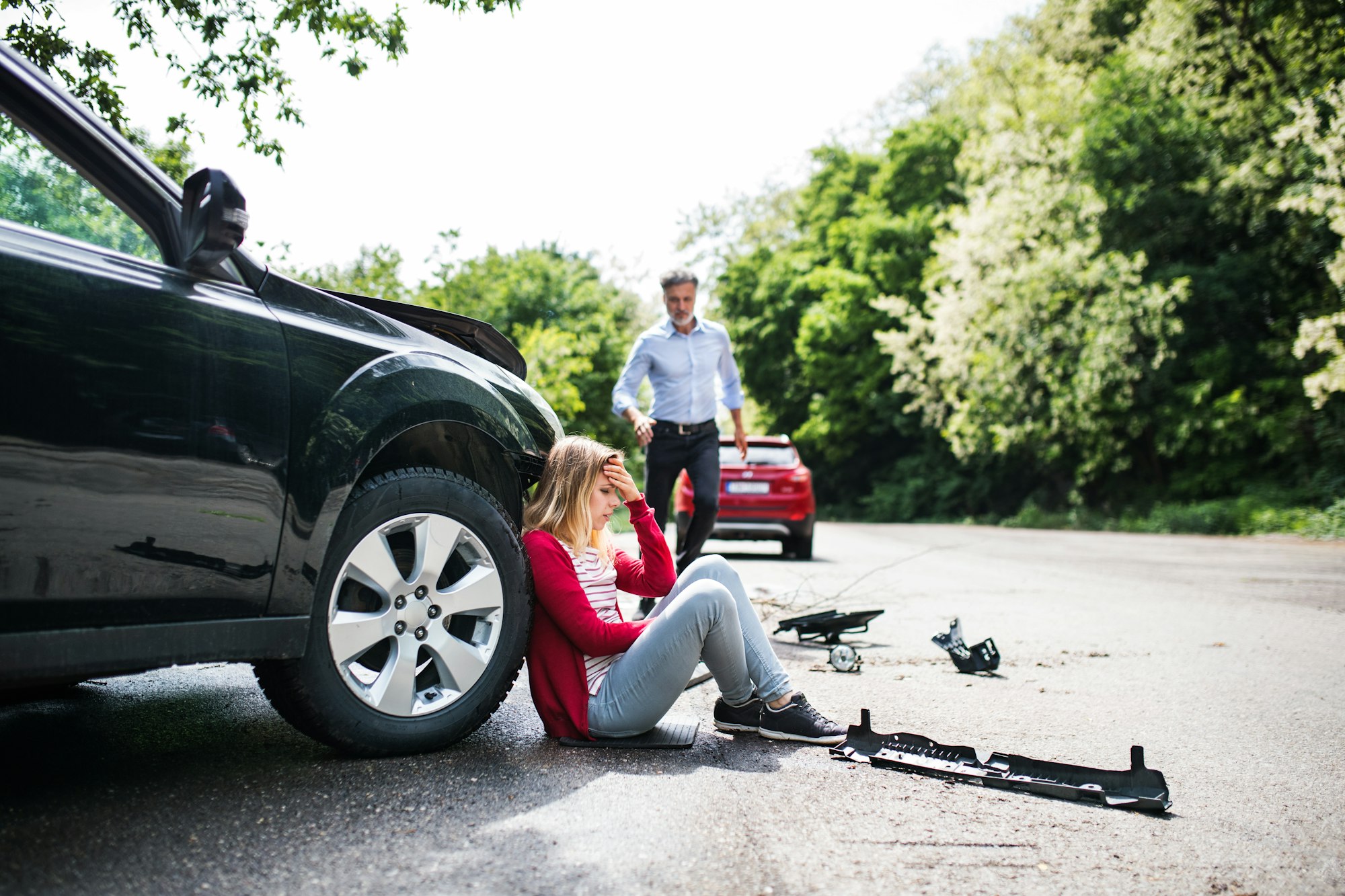 Young woman by the car after an accident and a man running towards her.