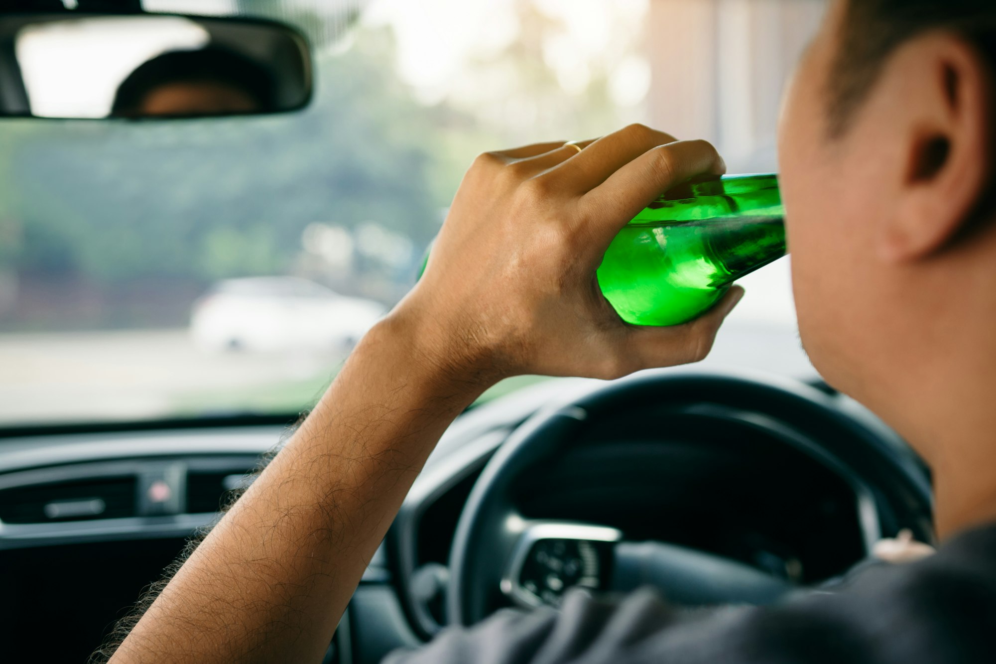 Asian men are breaking the traffic rules by holding a bottle of beer and drinking while driving.