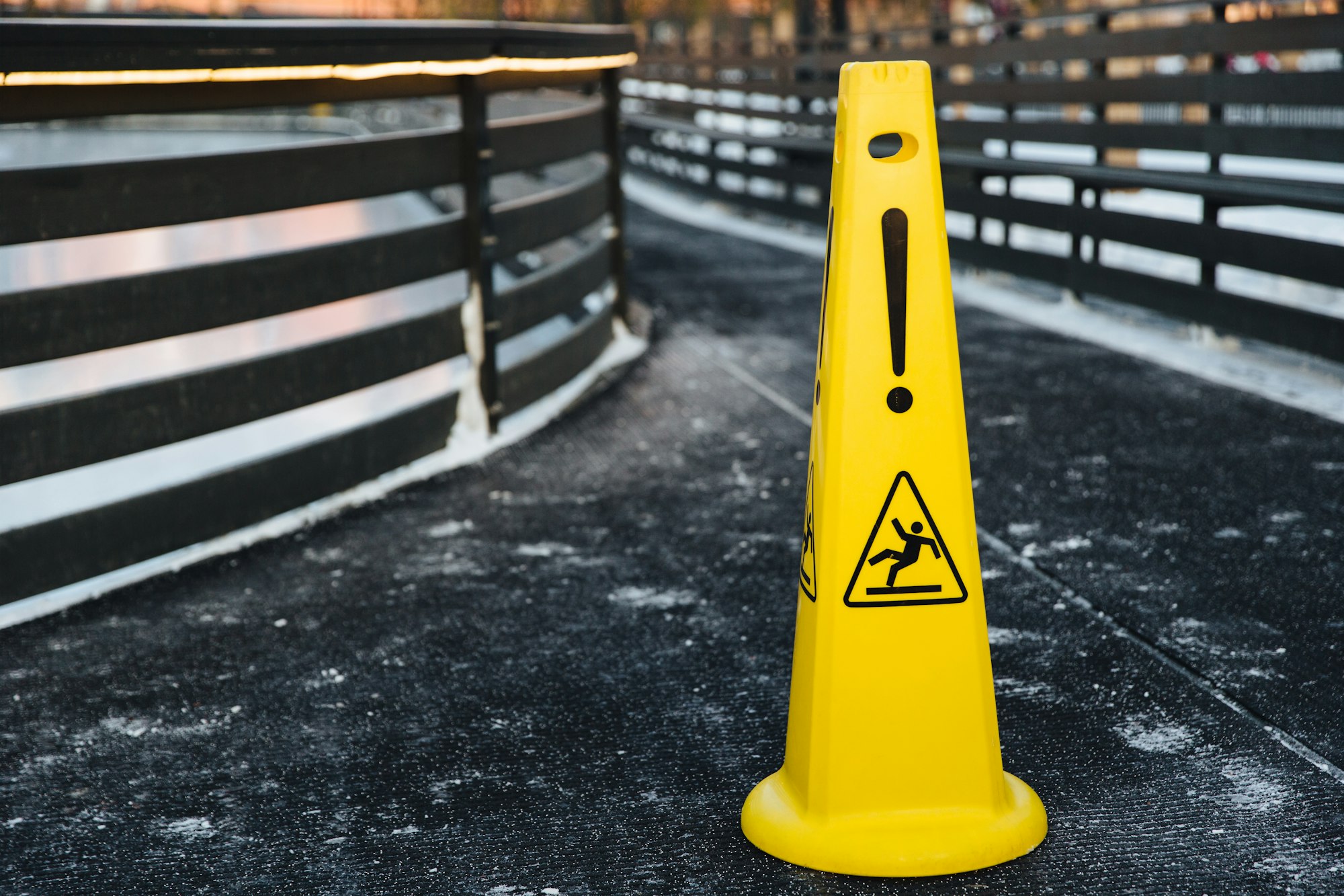 Close up shot of yellow warning sign stands on gray asphalt covered with snow