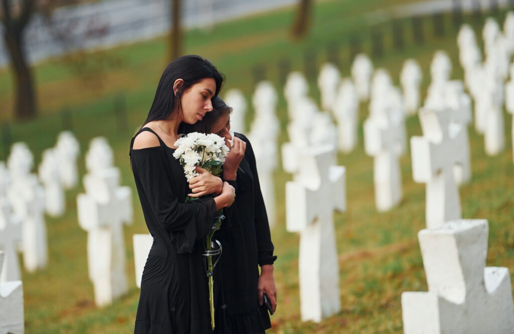 Two young women in black clothes visiting cemetery with many white crosses