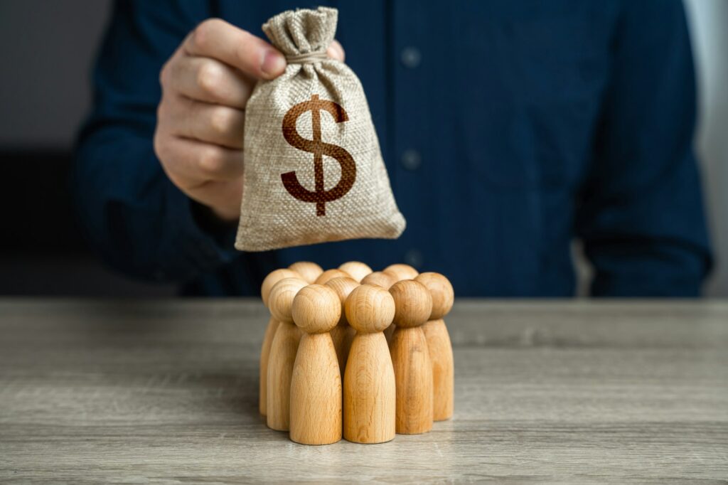 A man is holding a dollar money bag over a group of people figurines.