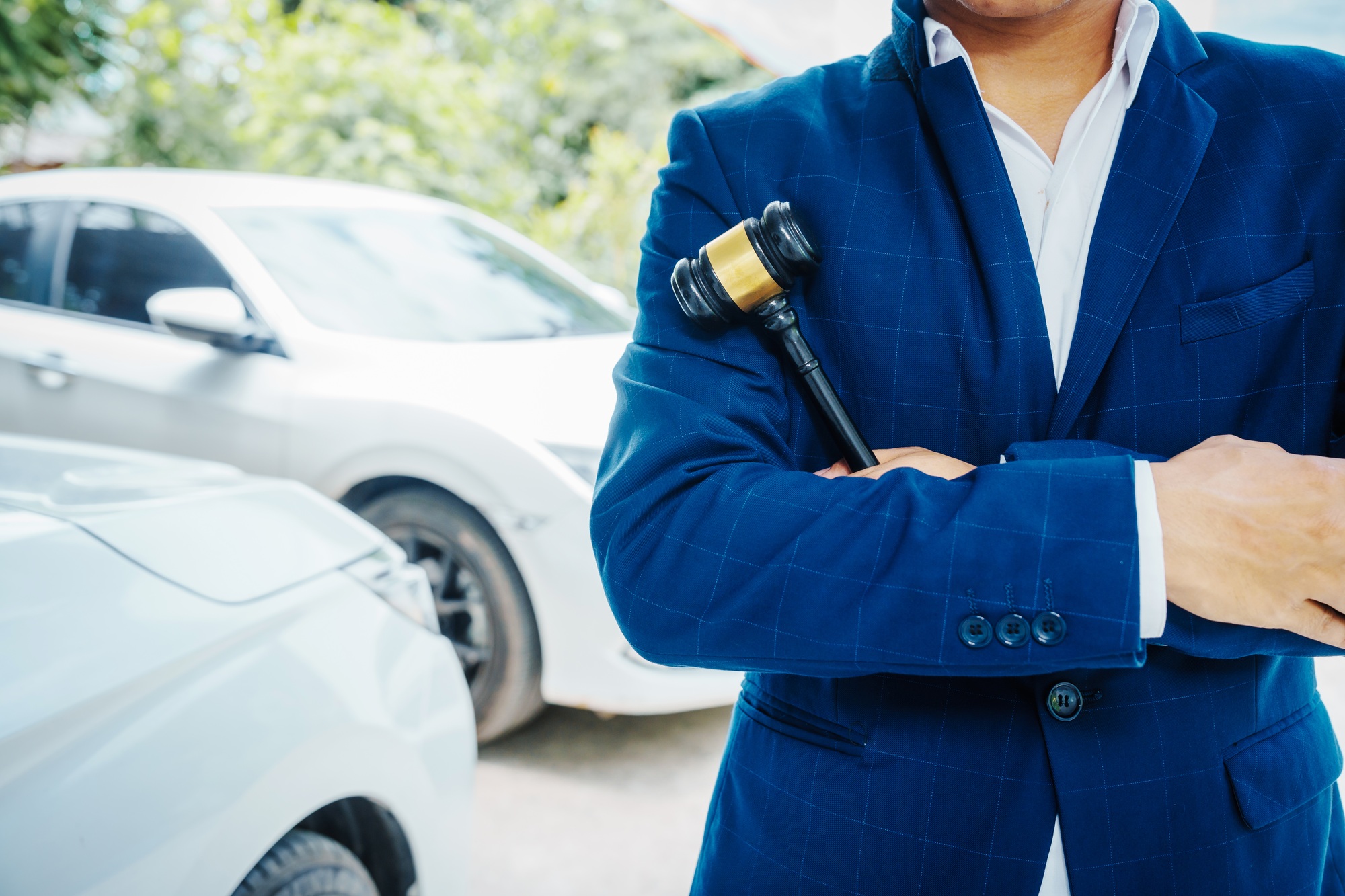 businessman in a suit and a lawyer, holding a wooden gavel, stand in front of a car
