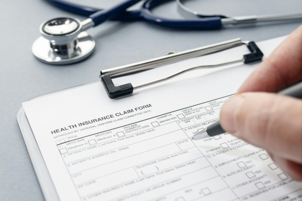 Hand filling on Health Insurance claim form on desk