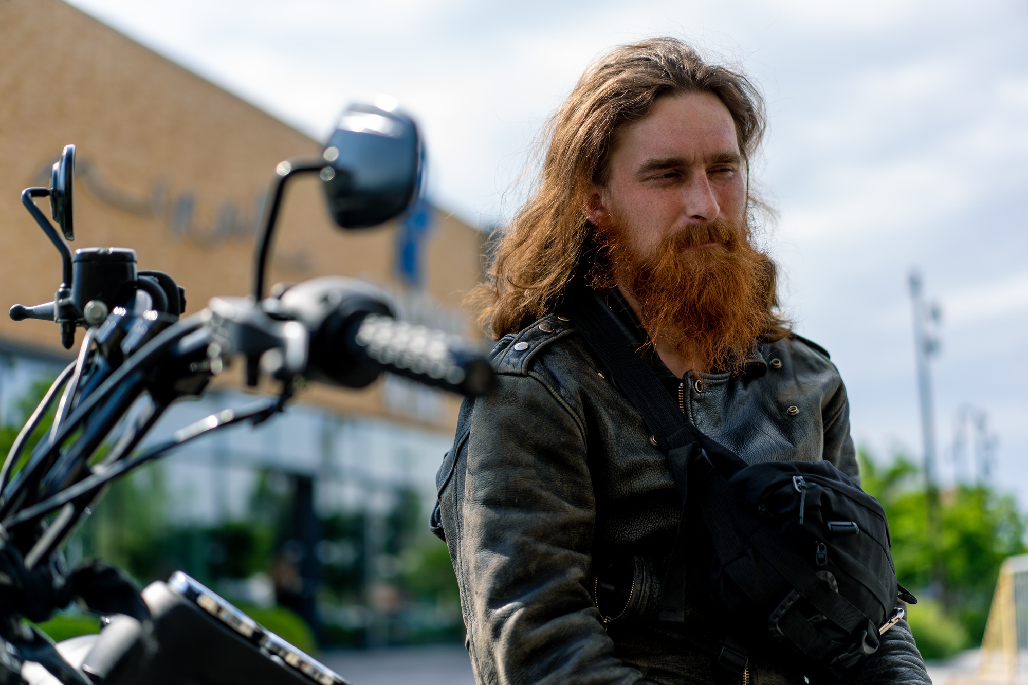 brutal thoughtful redhead bearded biker sitting on a black motorcycle after a race