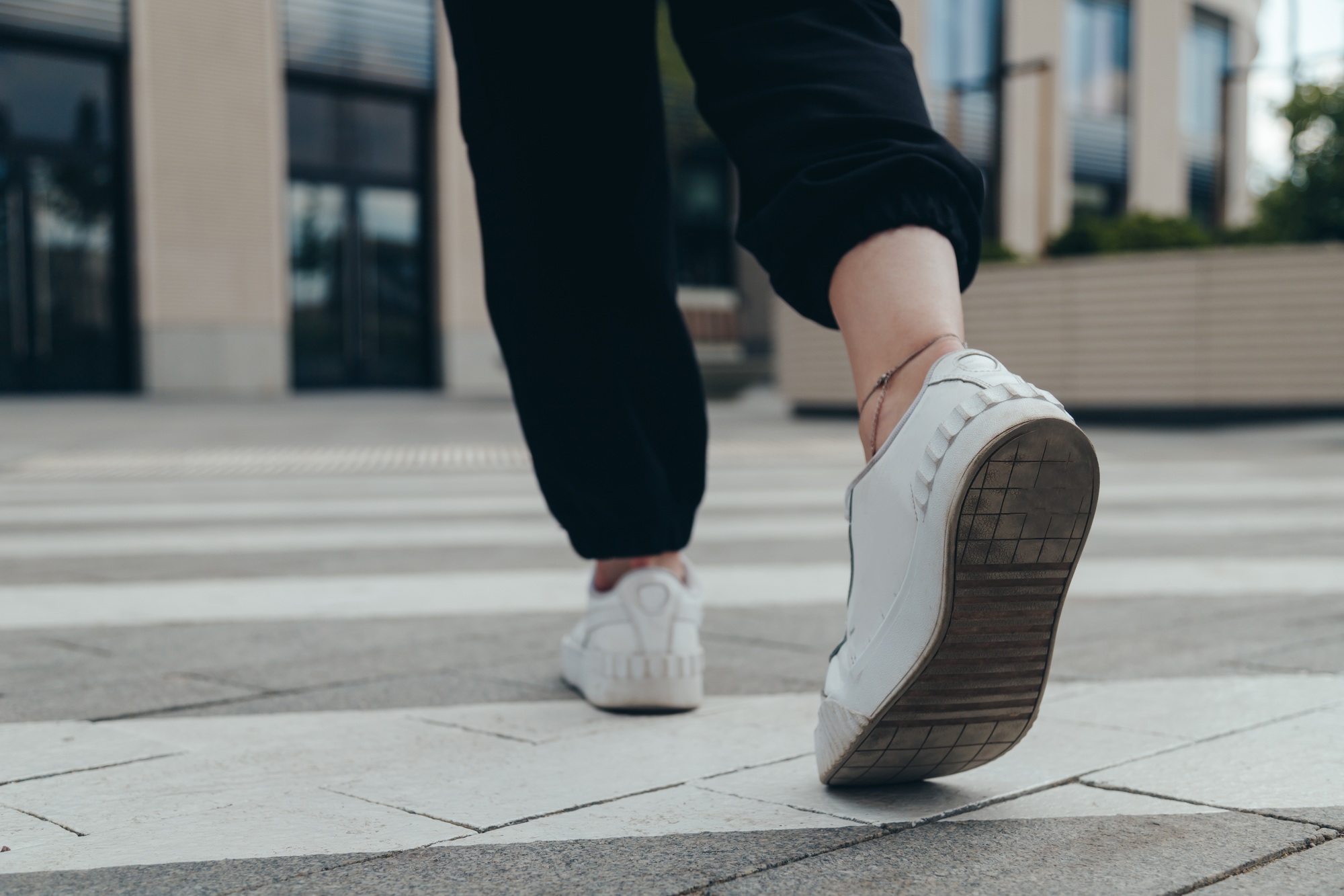 Legs of a girl in White Leather Sneakers Crosses the Street on a Pedestrian Crossing