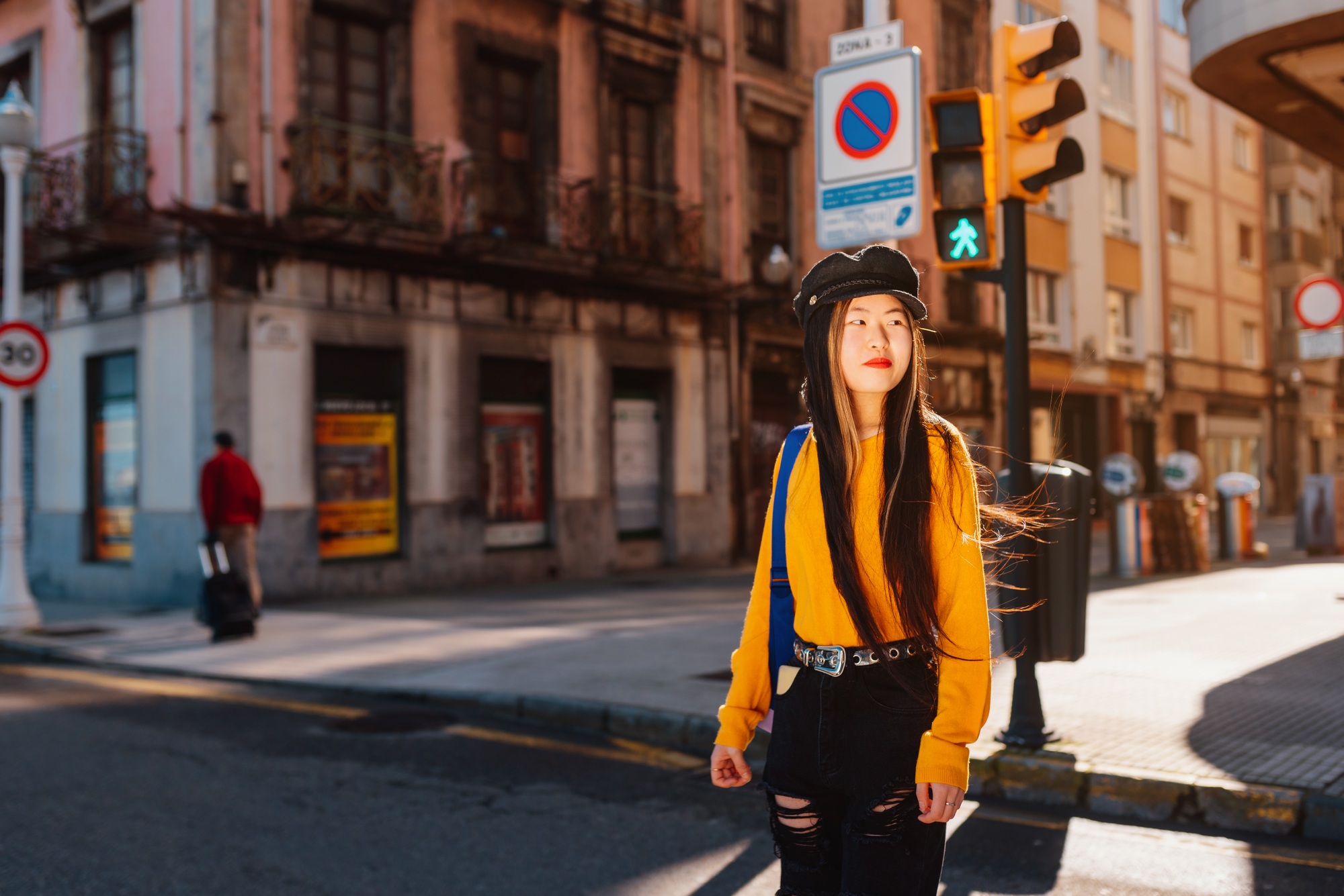 young asian woman crossing a pedestrian crossing in a european city while sightseeing in spain.