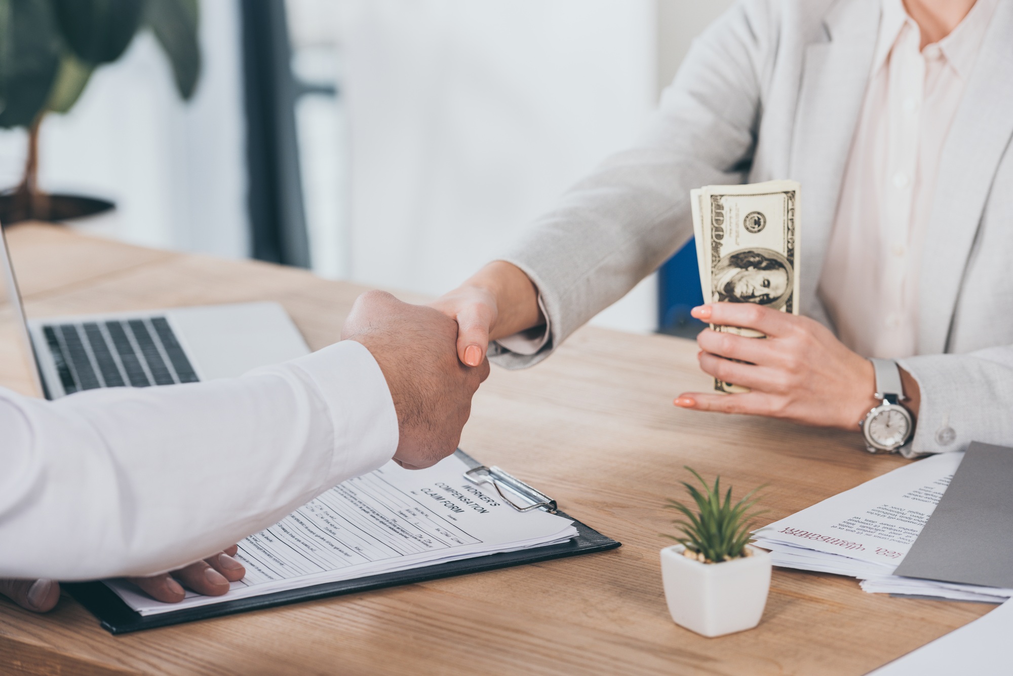 cropped view of businesswoman shaking hands with man and holding cash at workplace, compensation