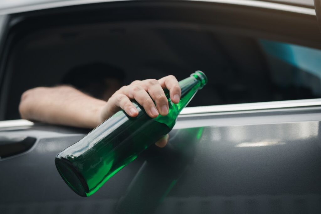 Asian man holding a bottle of beer outside the car while driving.