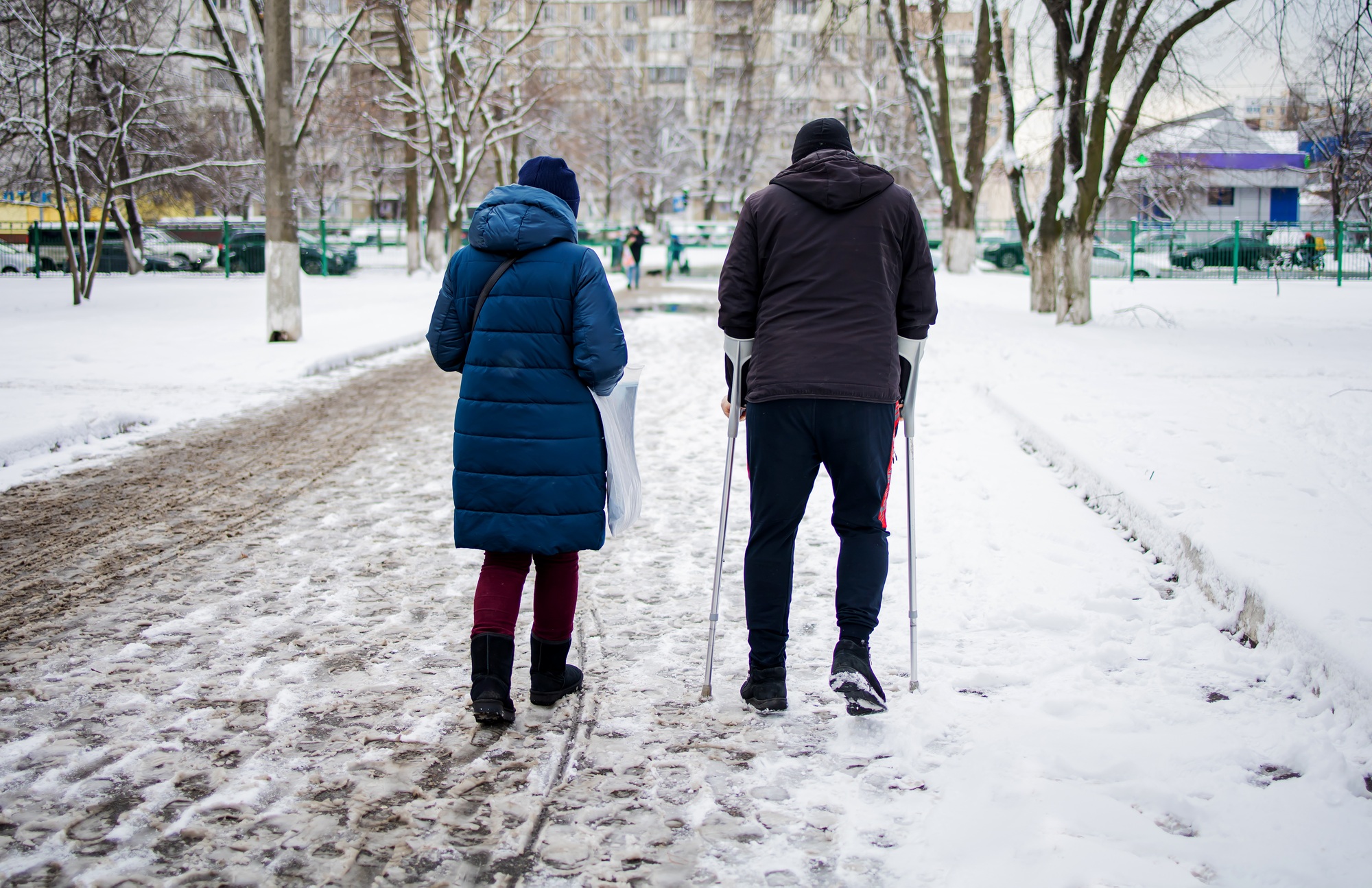 Poor Young Man with injured leg walking on winter slippery road. Road accident and rehabilitation co