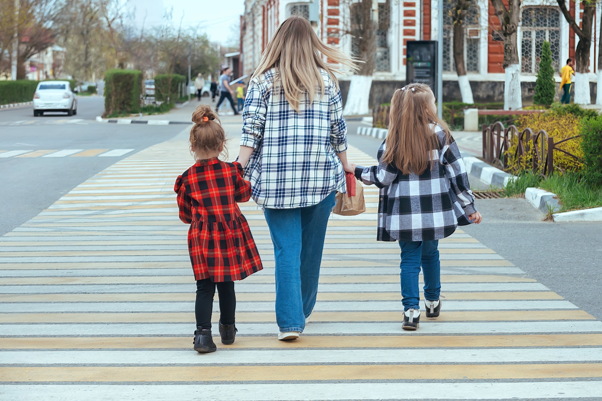 a family of three crosses the road on a car pedestrian crossing